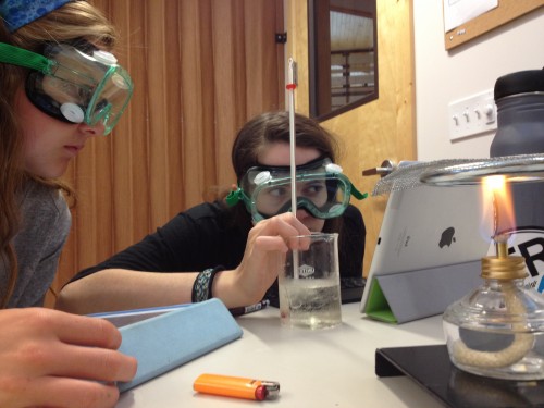 Elena and Estée prepare to move their beaker to the flame. 